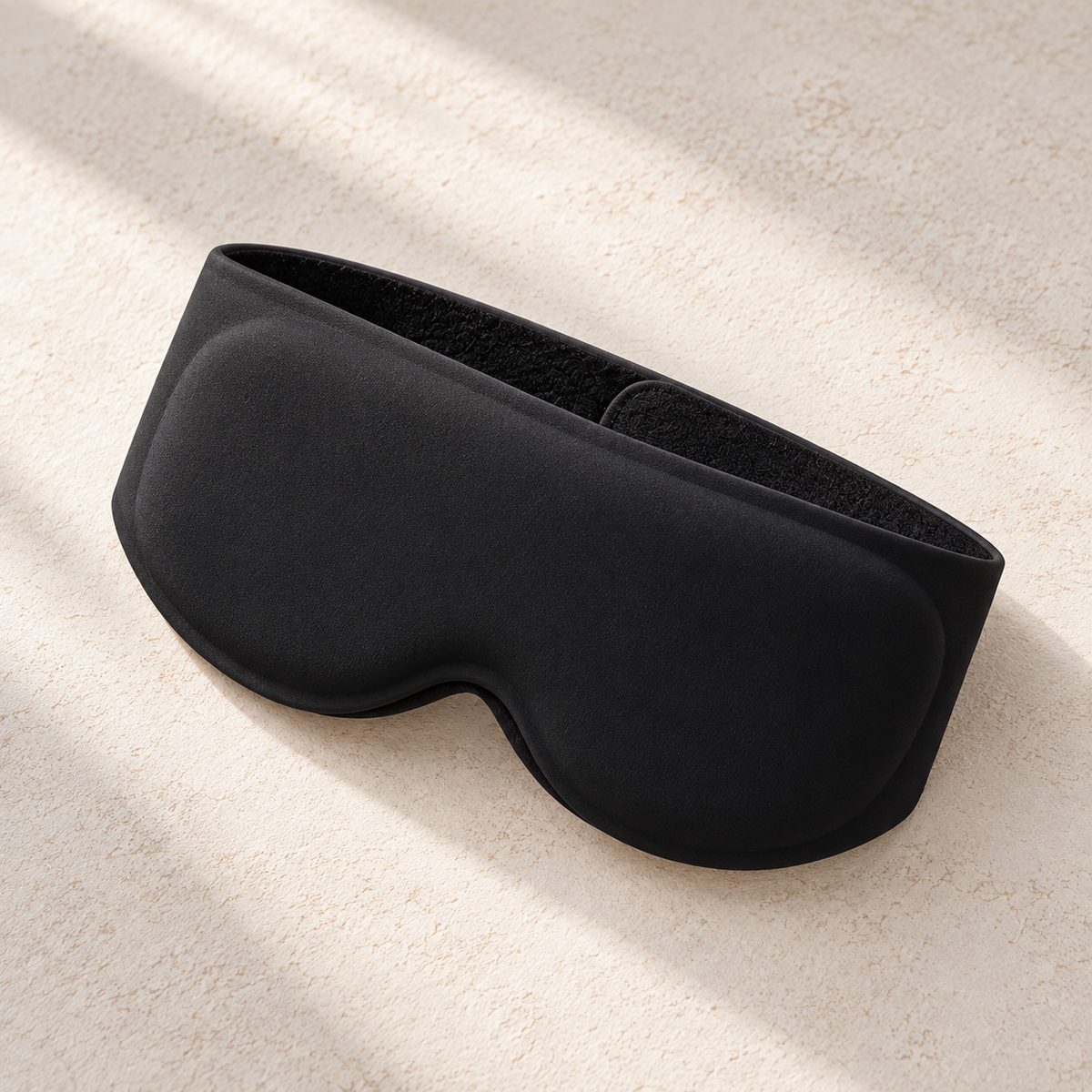 Black DreamCalm contoured weighted sleep mask on a warm neutral background